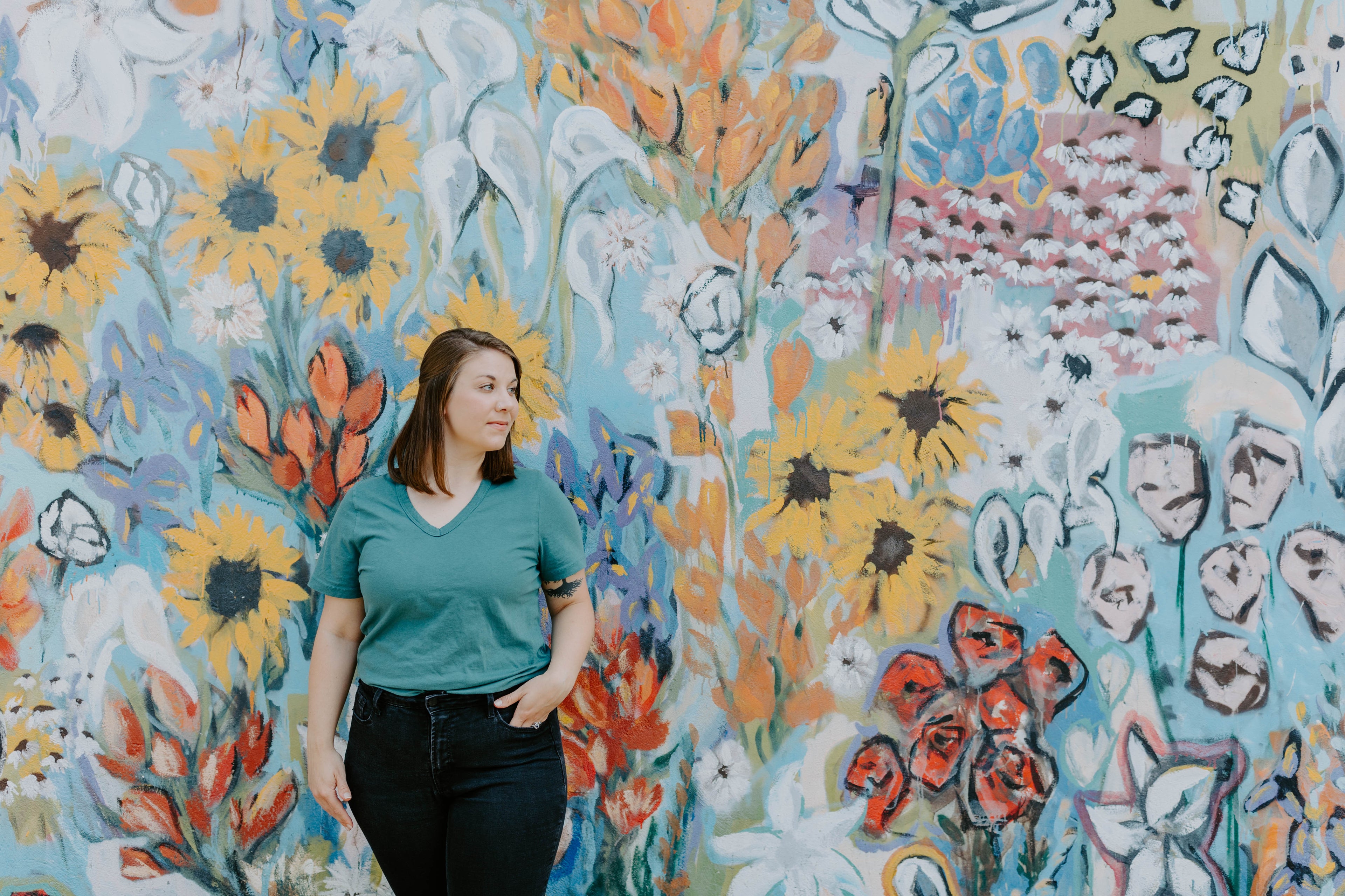 Amanda stands against a floral wall mural and looks to the right.