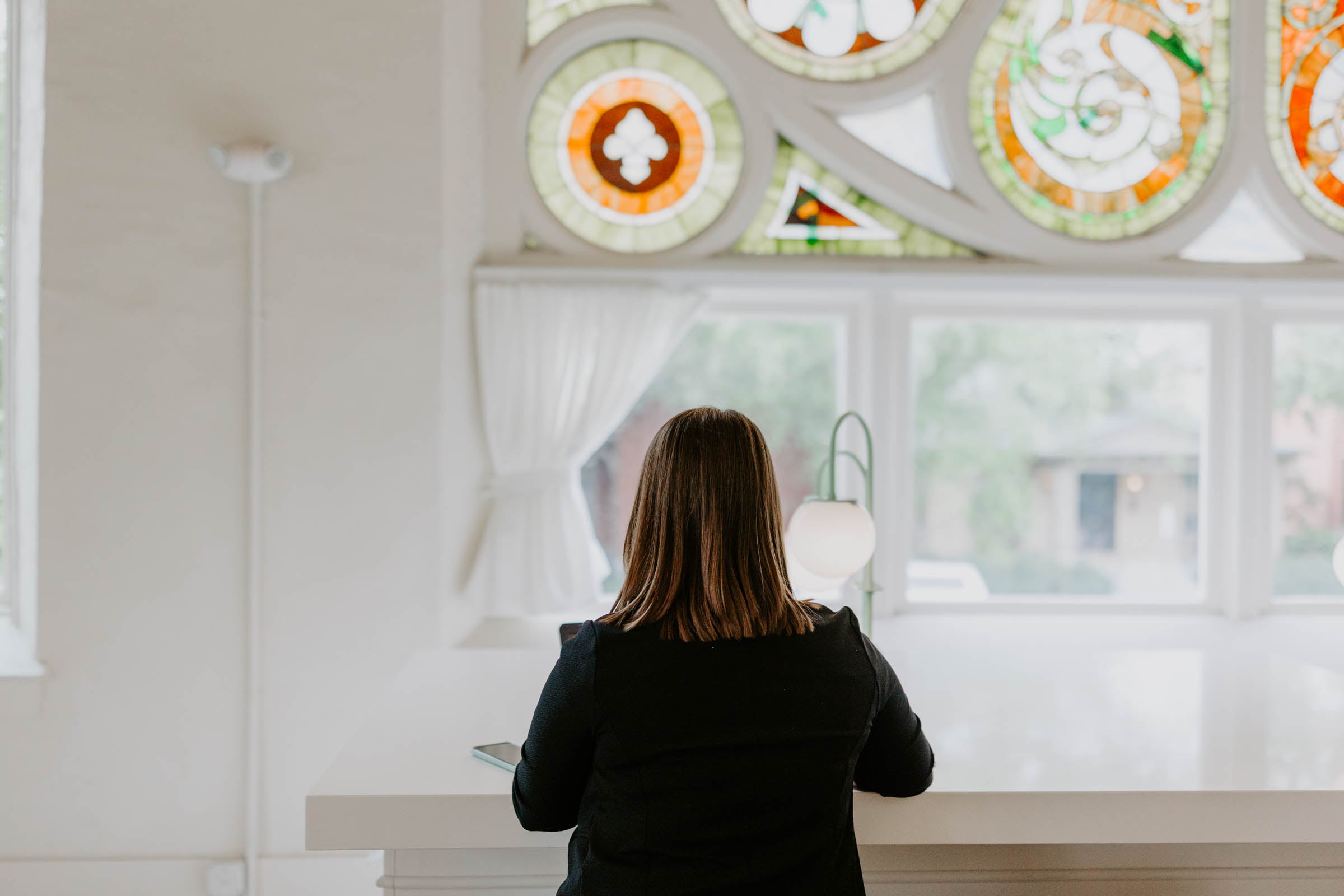 Amanda sits and writes at the bar of The Russel Boutique Hotel. Stained glass windows shine above her.